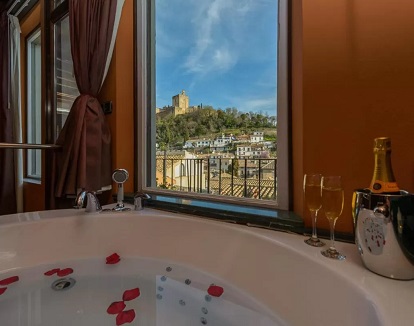 Jacuzzi, con pétalos rojos en el agua, para dos personas frente a la cama y con vistas a la Alhambra y con dos copas y una botella de Champagne